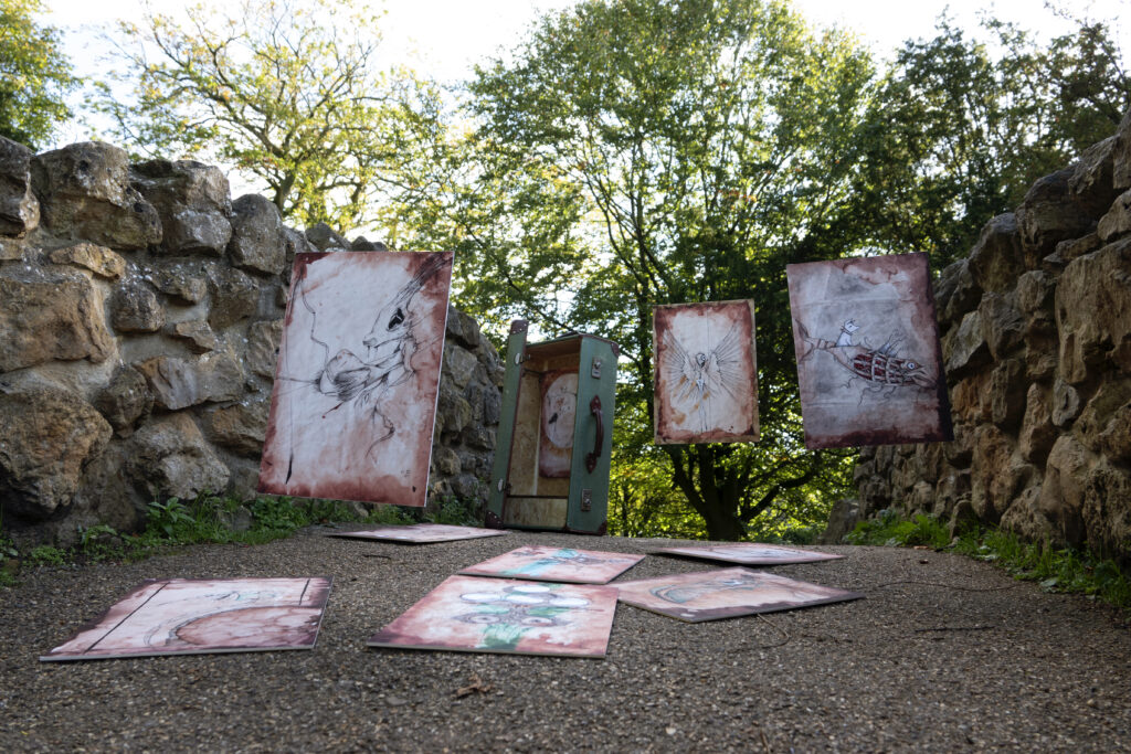 a vintage suitcase on a stone bridge in a park. The case is open and it appears to have character illustrations coming out of it. They can be seen suspended in the air and on the path.